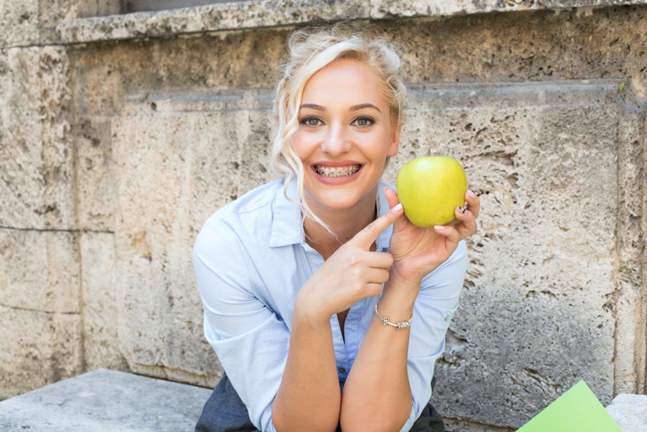 kobieta w aparacie na zębach trzymająca jabłko